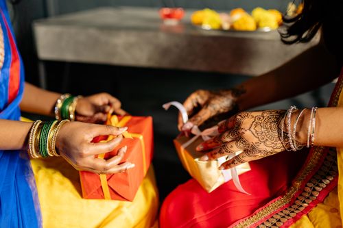 Free Two women in vibrant Indian attire exchange traditional gifts with henna designs. Stock Photo