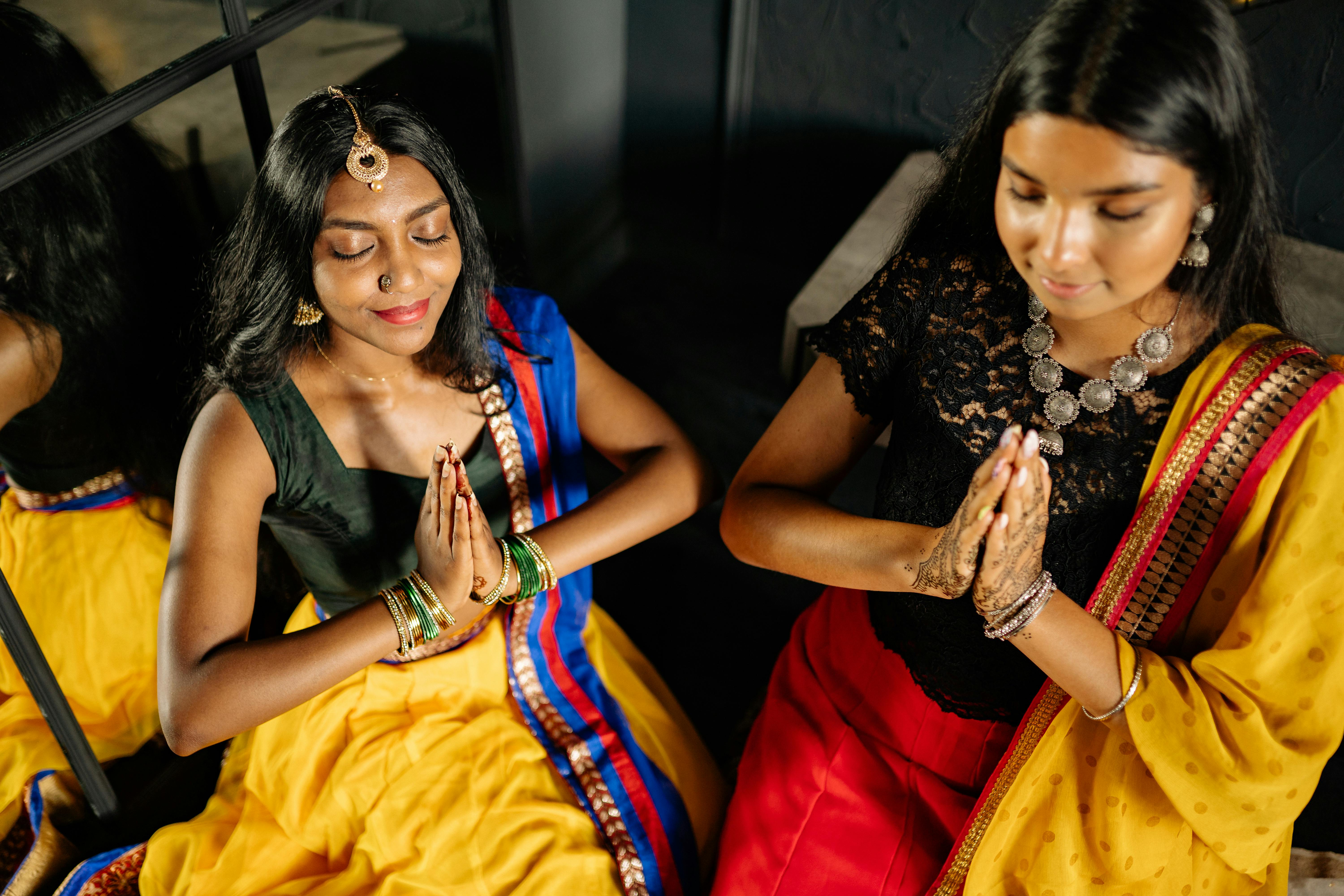 young women closing their eyes while praying in traditional saree dresses