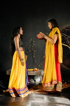 Two women in colorful traditional wear exchanging gifts during Diwali celebration.