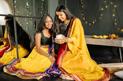 Women Wearing Sari Looking at the Screen of a Cellphone while Looking at Each Other