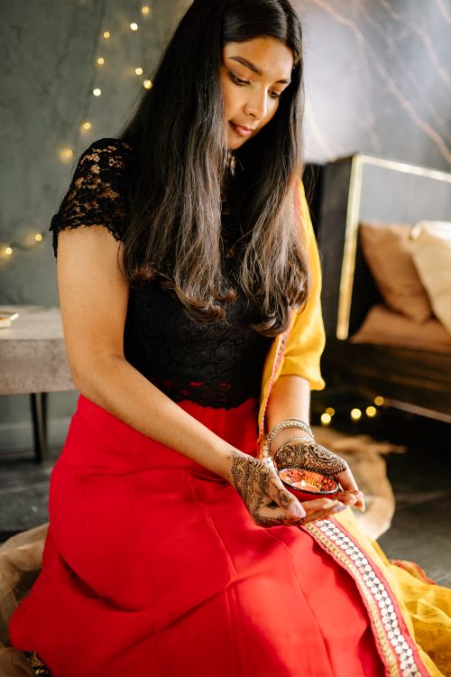 Free South Asian woman in traditional red attire holding henna candle, indoors with festive lighting. Stock Photo