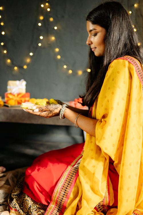 Free A young woman in traditional attire holds sweets during a cozy Diwali celebration indoors. Stock Photo