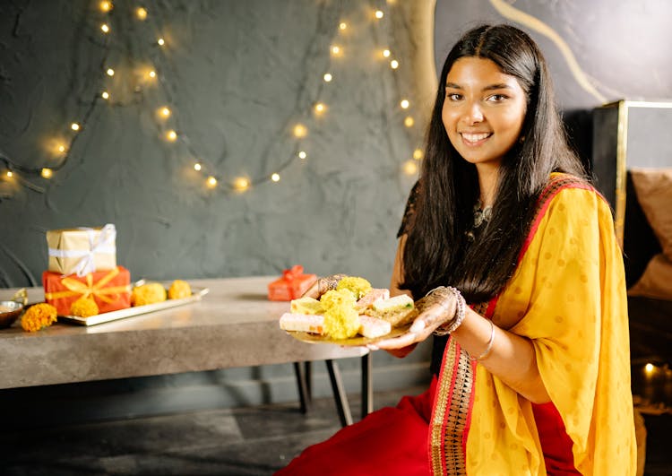 A Woman In Yellow And Red Sari Holding A Plate Of Food