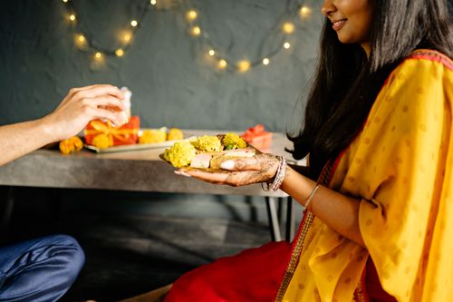 Free A woman holding a plate of Indian sweets during a festive celebration indoors. Stock Photo