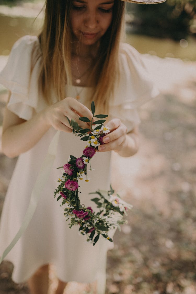 Young Woman In White Dress Braiding Flower Wreath On Head