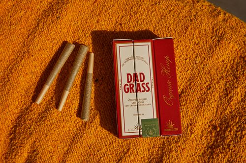 Free High-quality pre-rolled CBD joints and Dad Grass packaging on a vibrant surface. Stock Photo