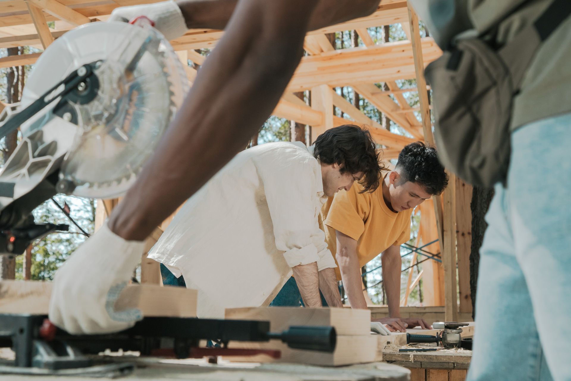 Workers using a circular saw on a sunny day at an outdoor construction site, collaborating on carpentry work.