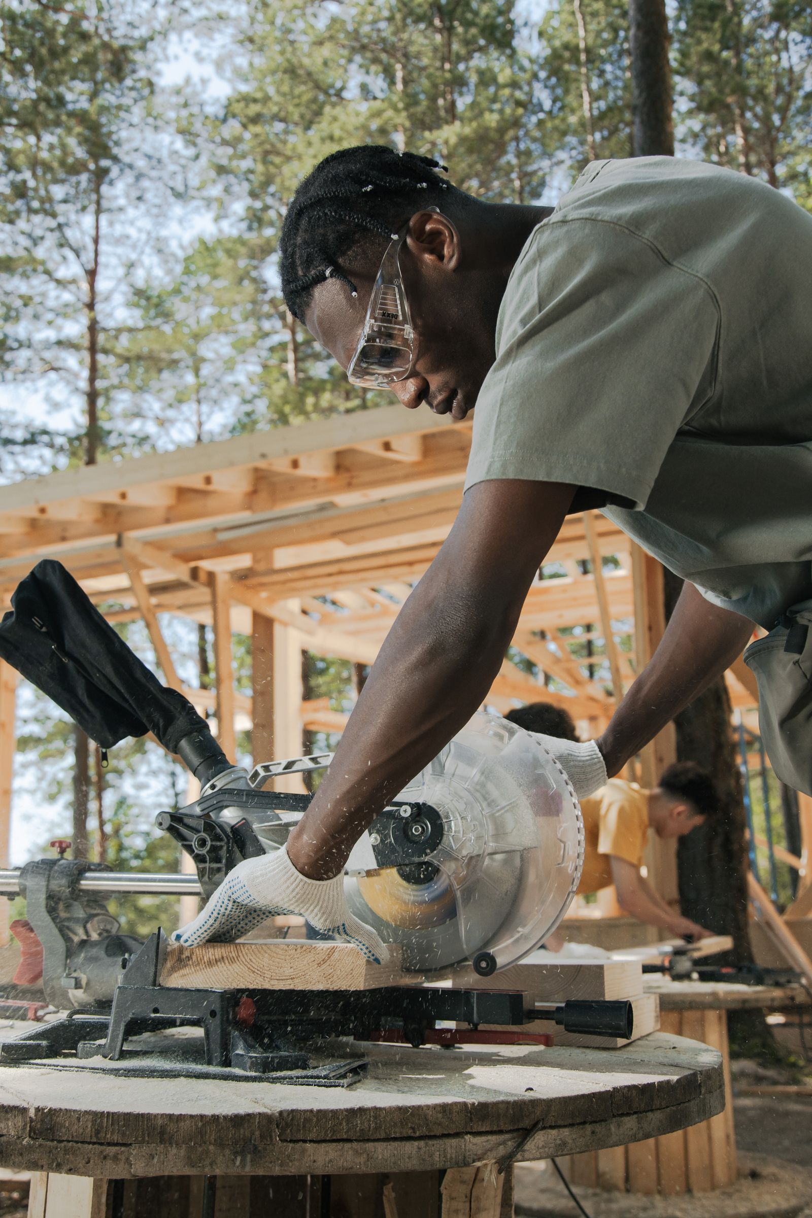 Worker wearing protective goggles and gloves operating a circular saw on timber