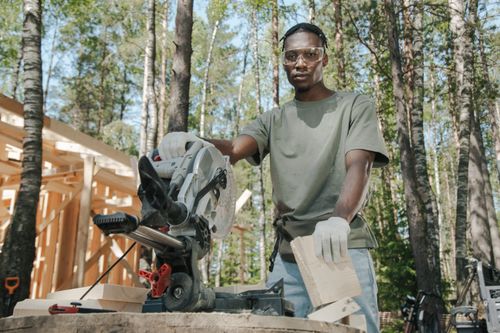 Free African American carpenter using a circular saw at a construction site in a forest. Stock Photo