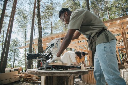 Free Workers on a construction site cutting wood planks with a circular saw outdoors. Stock Photo