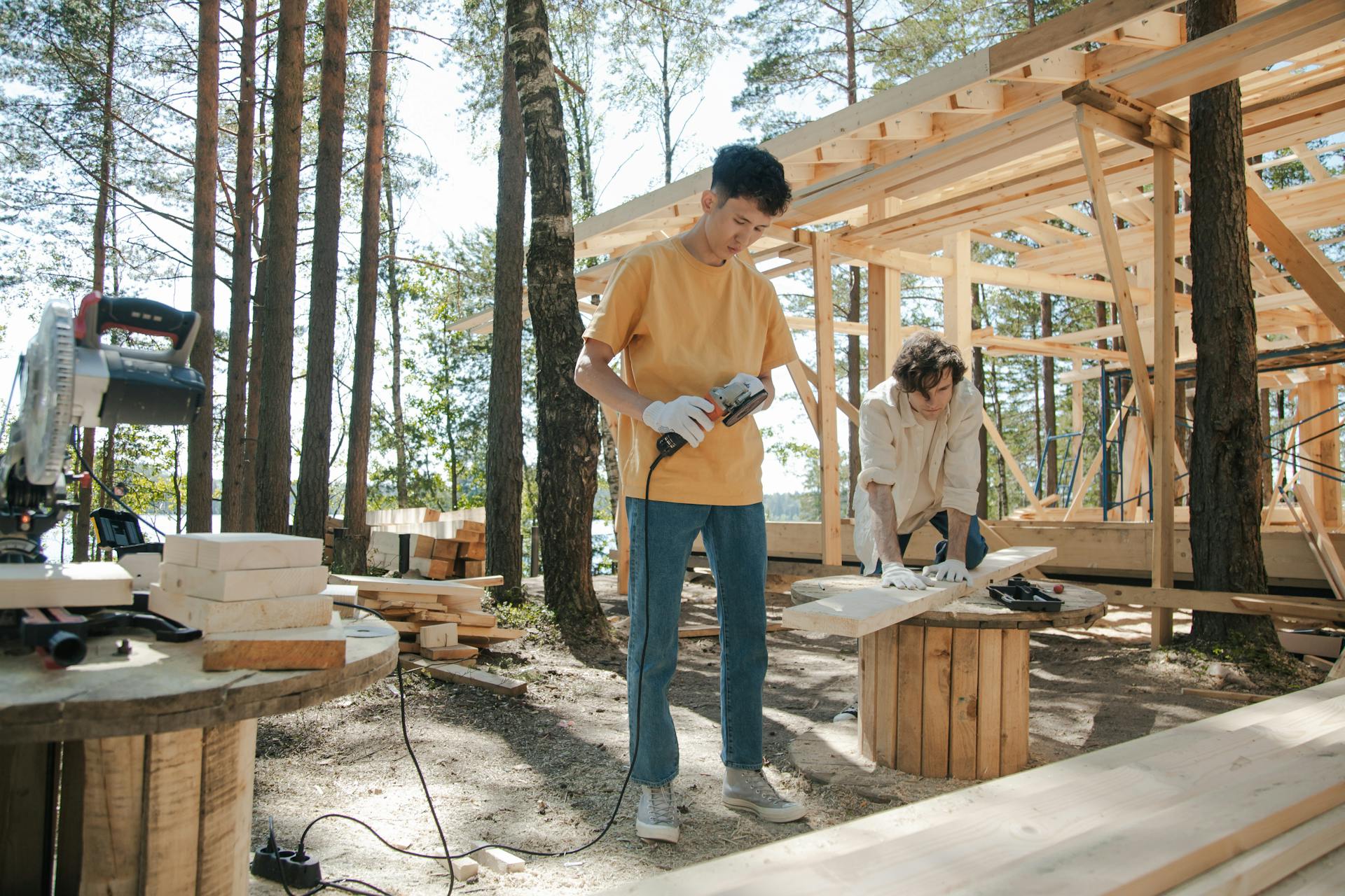 Two young men working on wooden construction project in forest setting.