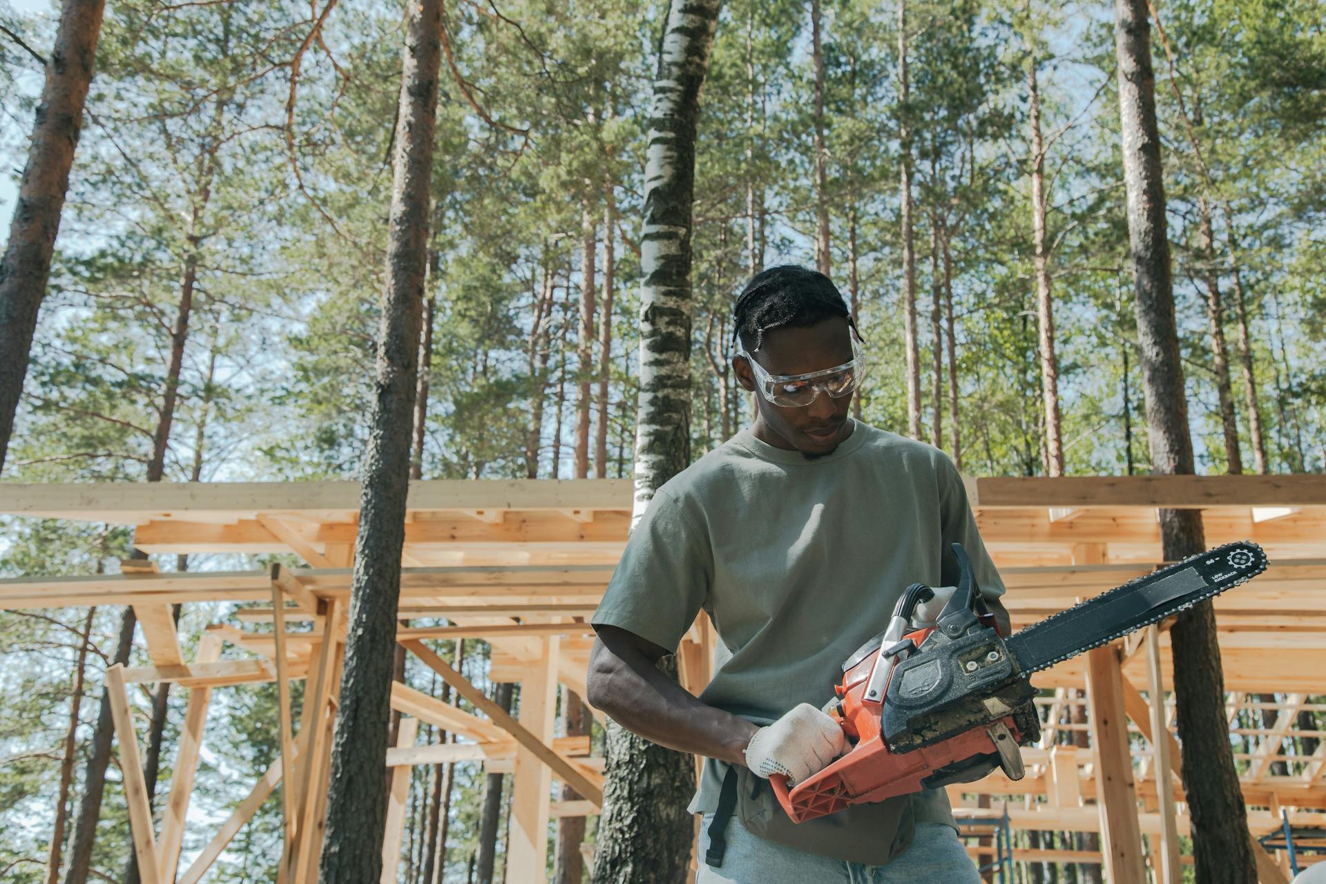 A man at a construction site in a forest, operating a chainsaw amidst tall trees.