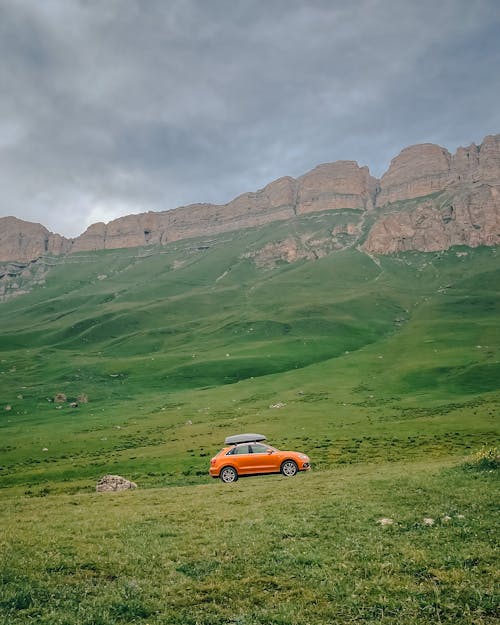 Free Orange Car with Roof Rack in Green Mountain Landscape Stock Photo