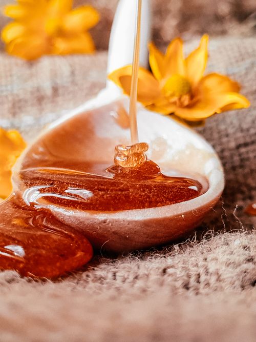 Free Golden honey dripping from a spoon with yellow flowers for a natural, sweet aesthetic. Stock Photo