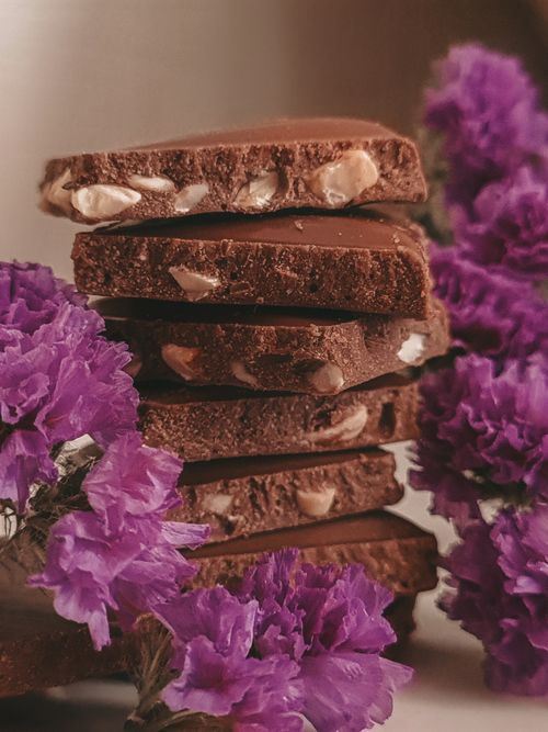 Free A close-up of chocolate bars with nuts, surrounded by vibrant purple flowers. Stock Photo