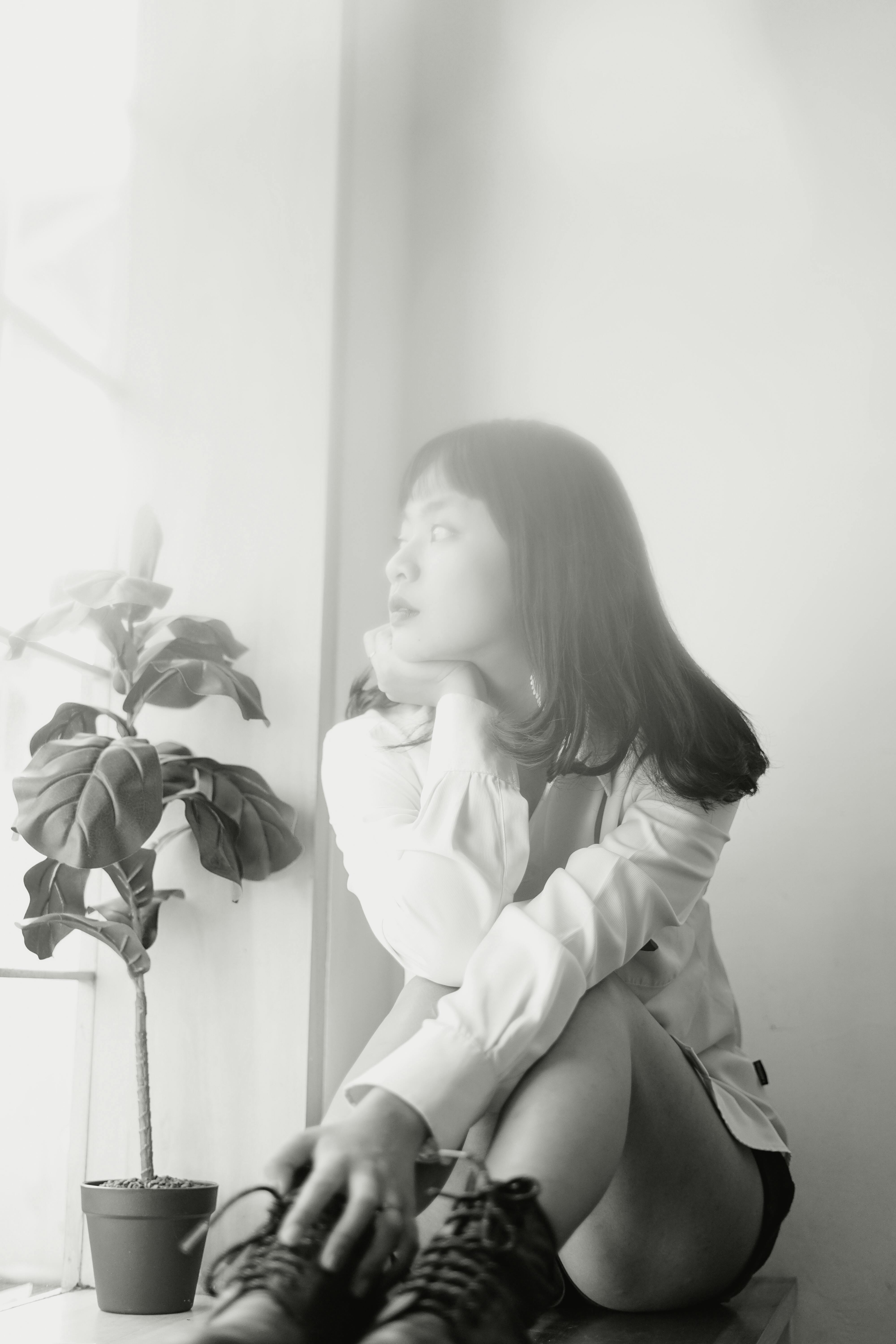 Black and white portrait of a seated woman gazing thoughtfully out of a window.