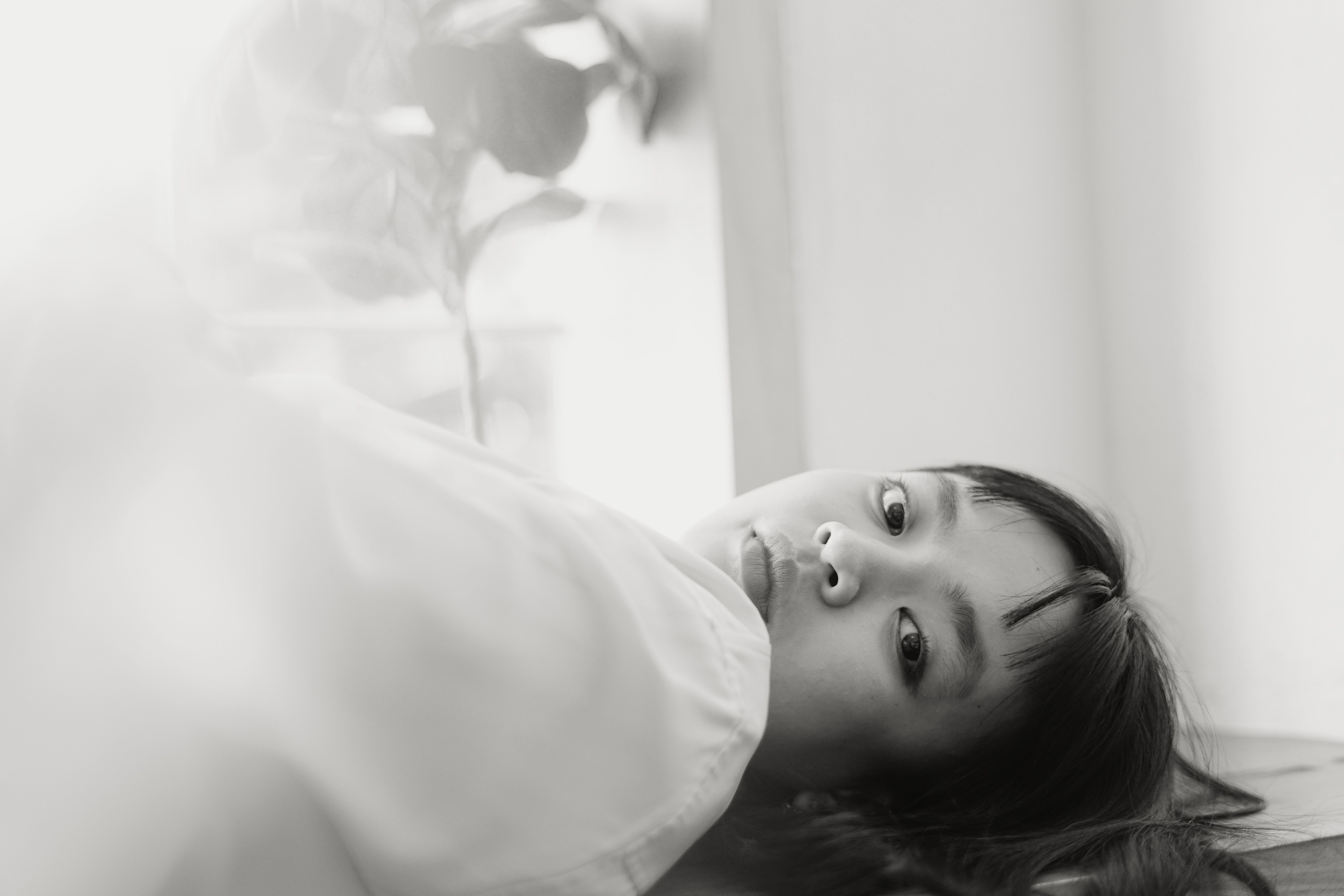 Black and white portrait of a young woman lying indoors looking contemplatively.
