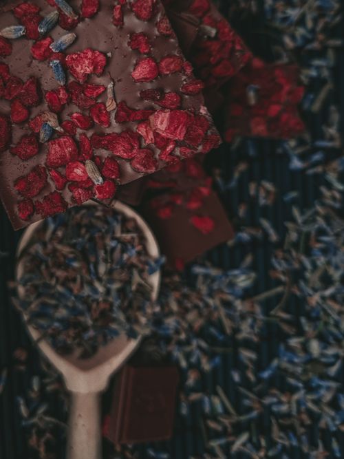 Free Rich dark chocolate topped with vibrant red berries and lavender on a rustic background for a gourmet look. Stock Photo