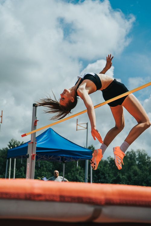 Free Dynamic shot of a female athlete clearing the bar during a high jump event outside. Stock Photo