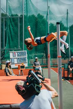 Female athlete performs a high jump at an outdoor sporting event on a sunny day.