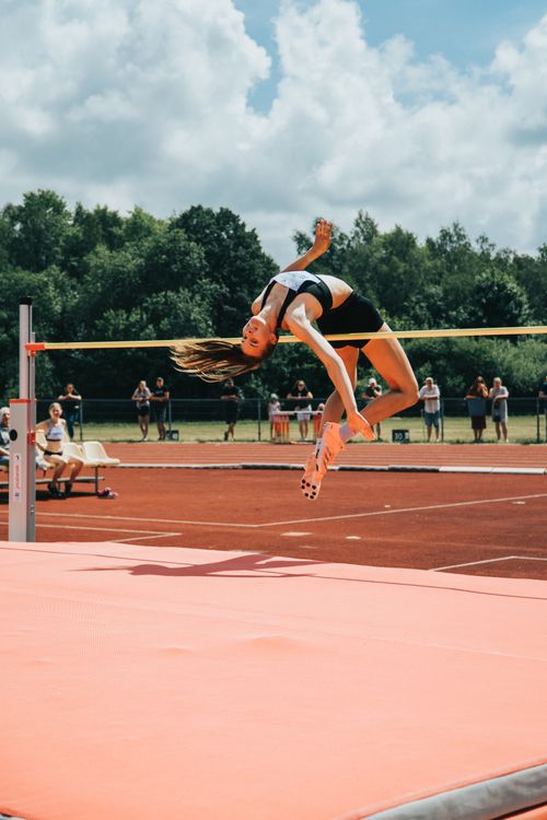 Free A female athlete in midair performing a high jump at an outdoor track and field event. Stock Photo