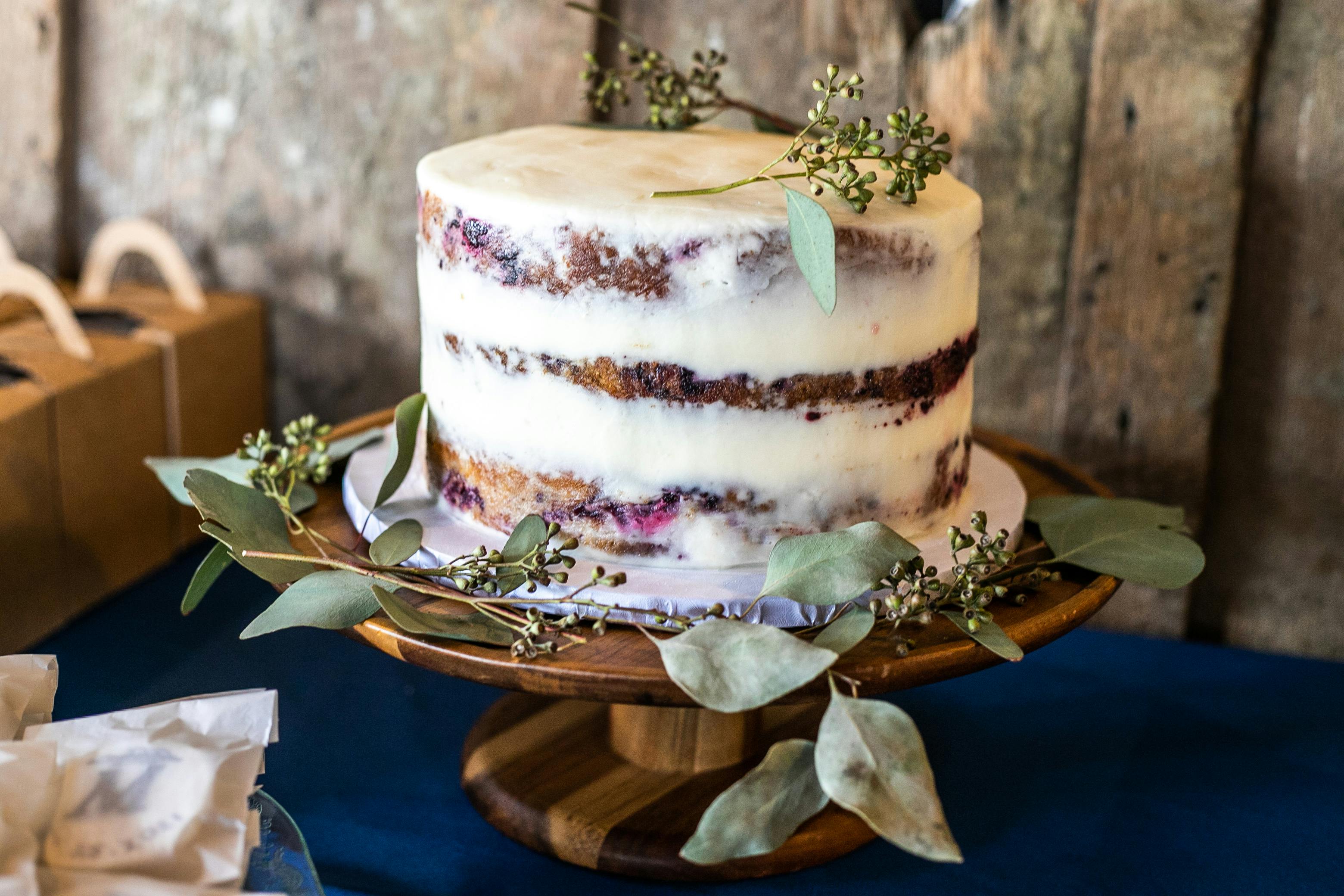 A rustic naked cake adorned with fresh greenery on a wooden cake stand, perfect for weddings or celebrations.
