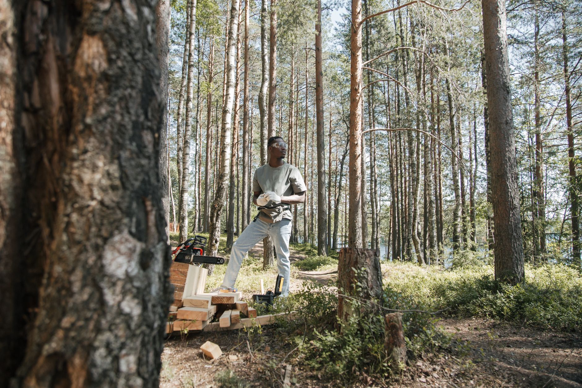 African American man with chainsaw working in a bright forest clearing during the day.