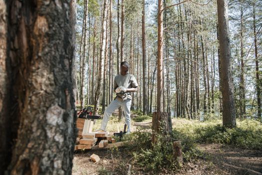 African American man with chainsaw working in a bright forest clearing during the day.