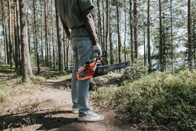 Ouvrier tenant une tronçonneuse dans une forêt ensoleillée, matériel de motoculture