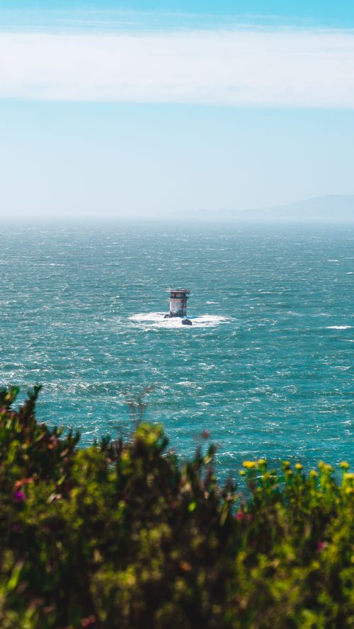 Free Picturesque lighthouse surrounded by ocean with vibrant plants in foreground. Stock Photo