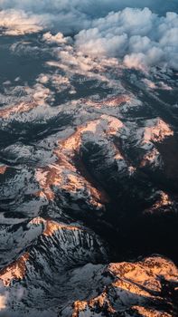Stunning aerial view of a snow-covered mountain range with dramatic sunlight and clouds.