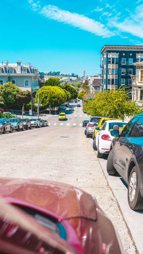 Free Colorful city street lined with parked cars under a bright blue sky, showcasing urban life. Stock Photo