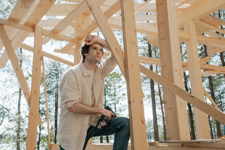 A Man Leaning On A Wooden House Frame