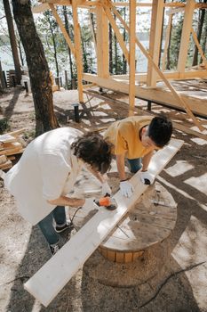 Two adults woodworking outdoors, using power tools on a wooden plank.