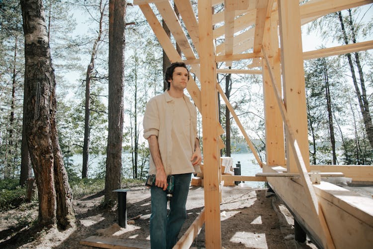 Man Standing Beside A House Frame Holding A Power Tool