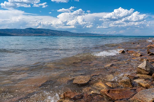 A beautiful rocky shoreline with waves under a vibrant blue sky and fluffy clouds.