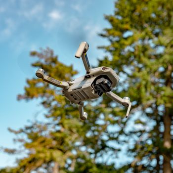 Flying drone captured mid-air against a scenic forest backdrop, showcasing modern technology outdoors.