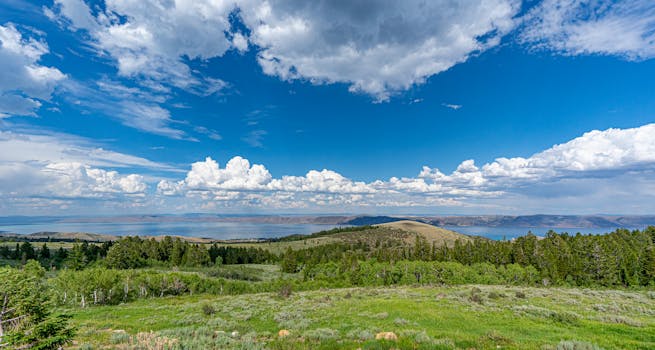Stunning landscape of a lake surrounded by mountains with a vibrant blue sky and fluffy clouds.