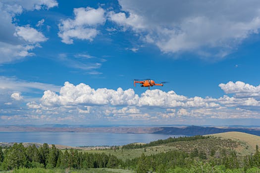 Orange drone capturing stunning views over a lake with hills and a blue cloudy sky.