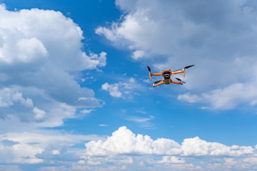 Drone flying mid-air against a vibrant blue sky with fluffy clouds, showcasing modern technology and aerial photography.