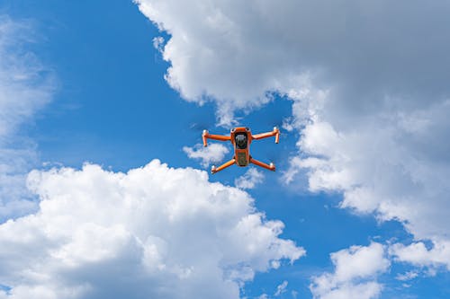 Free 
An Orange Drone Flying under a Cloudy Sky Stock Photo