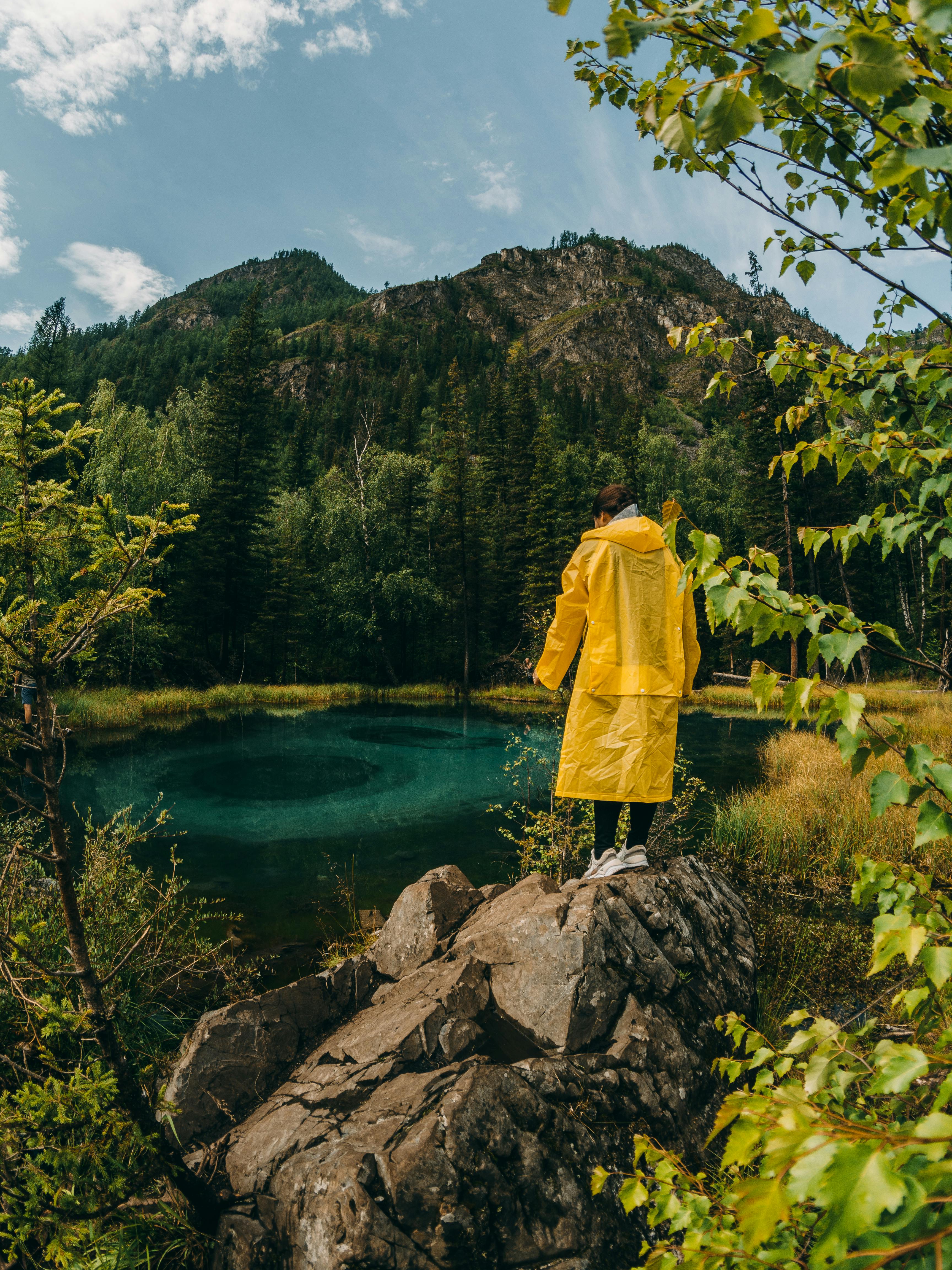 Person Wearing Yellow Raincoat Standing on Big Rock Free Stock Photo