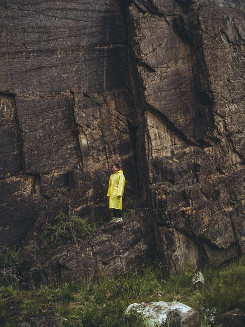 A person in a yellow raincoat stands by a rugged rock wall in the Altai Republic, showcasing nature's raw beauty.