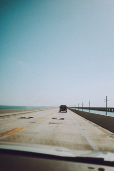 A vehicle travels across an expansive concrete bridge over the ocean on a clear day.