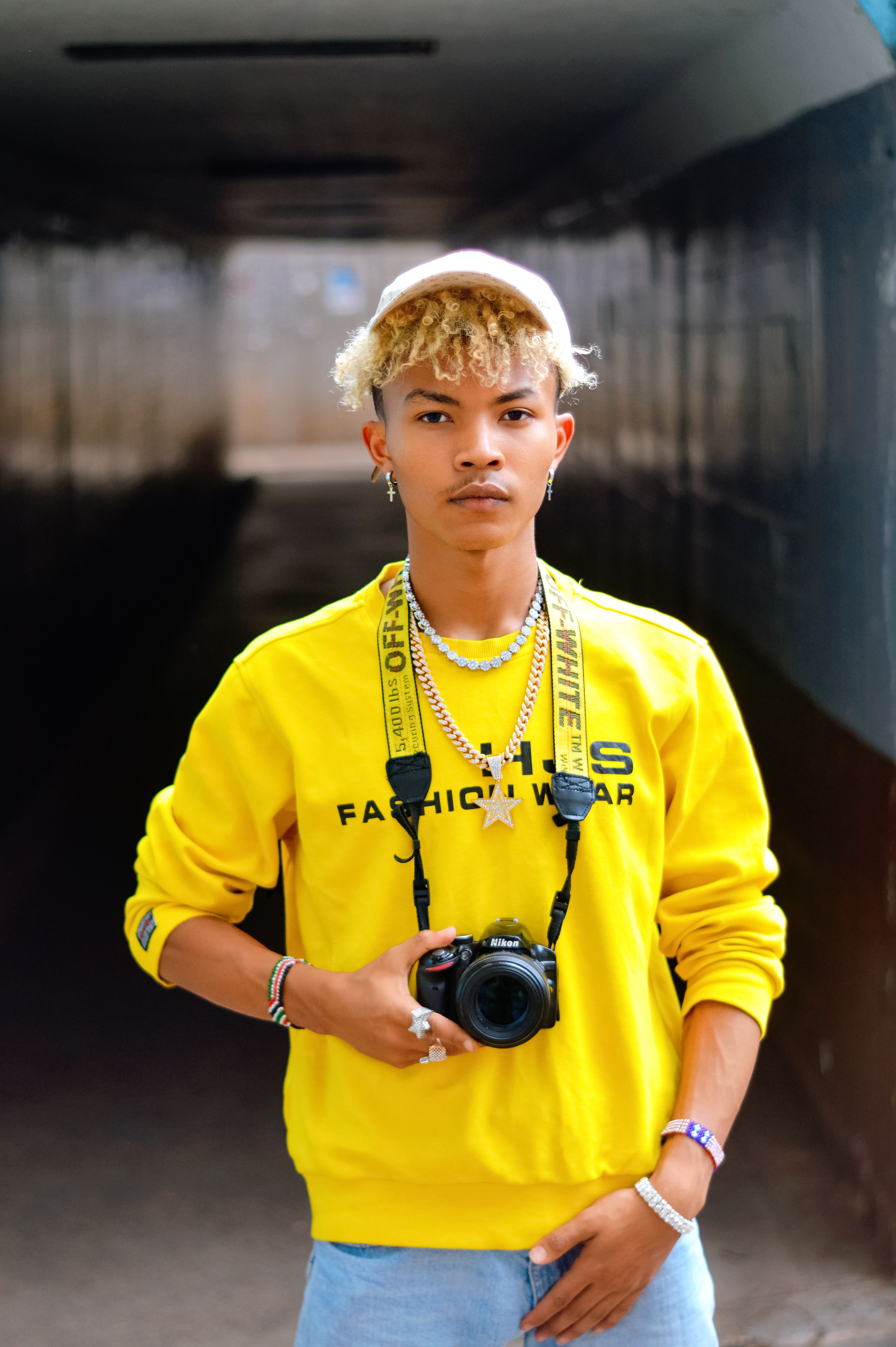 Portrait of a trendy young man with curly hair holding a camera in an urban setting.
