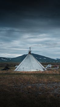 A solitary tent in an open field under a dramatic, cloudy sky, suggesting remote camping or adventure.