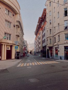 Empty city street with pedestrian crossing, surrounded by classic buildings.