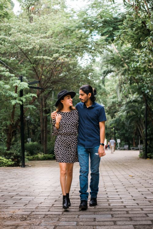 Free Young couple embracing while walking through a scenic park path surrounded by greenery. Stock Photo