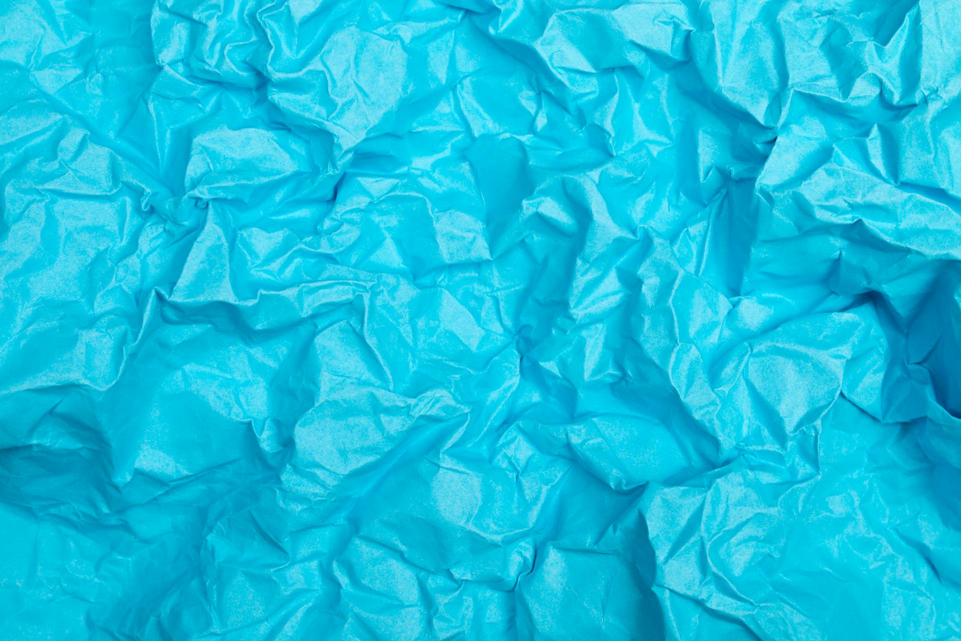 Vivid crumpled light blue paper texture with abstract appearance.