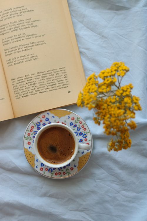 Free Top view of a coffee cup with a patterned saucer, an open book, and yellow flowers on a white surface. Stock Photo